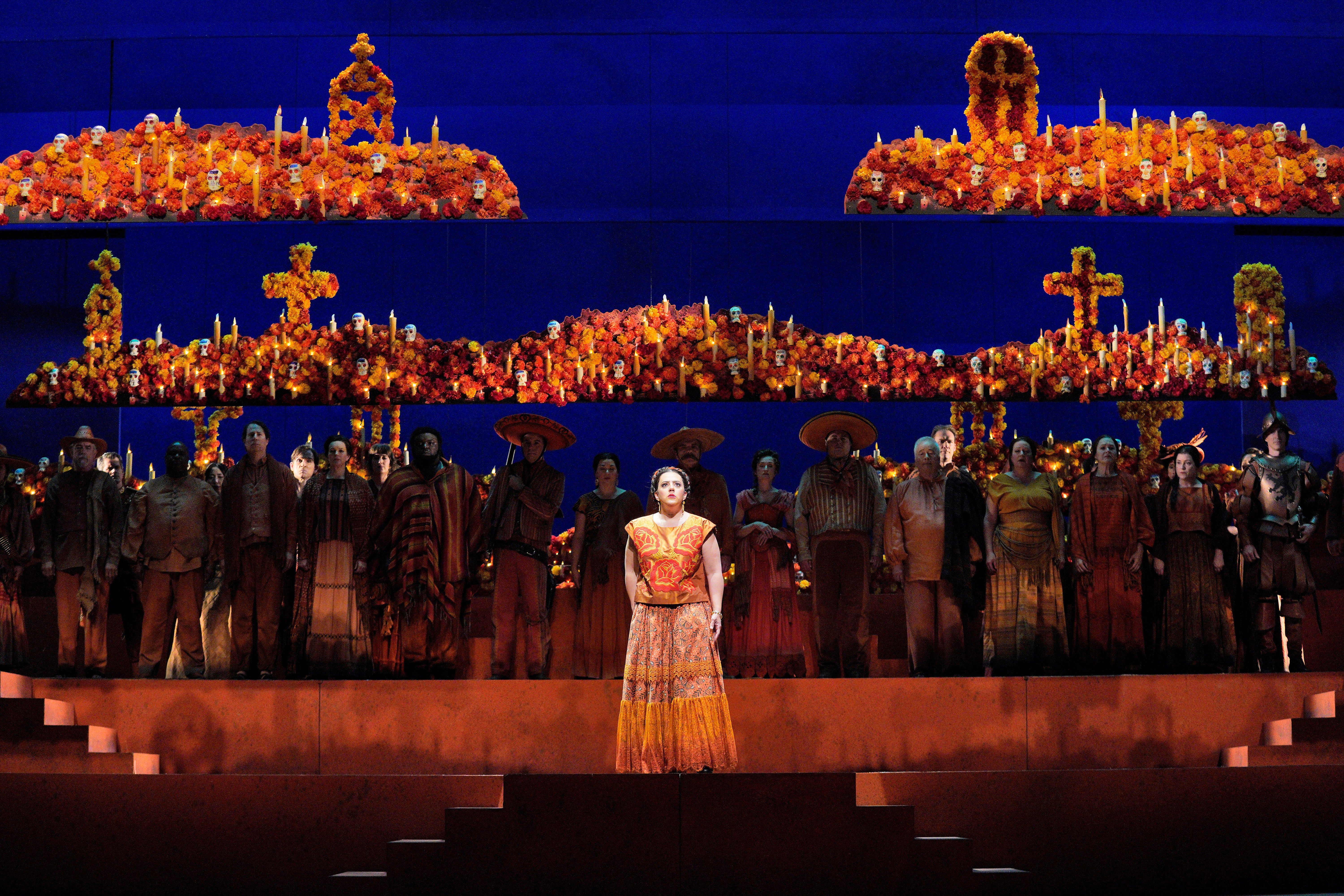 Scene from Frida A woman is standing on stage in front of a large group of people.