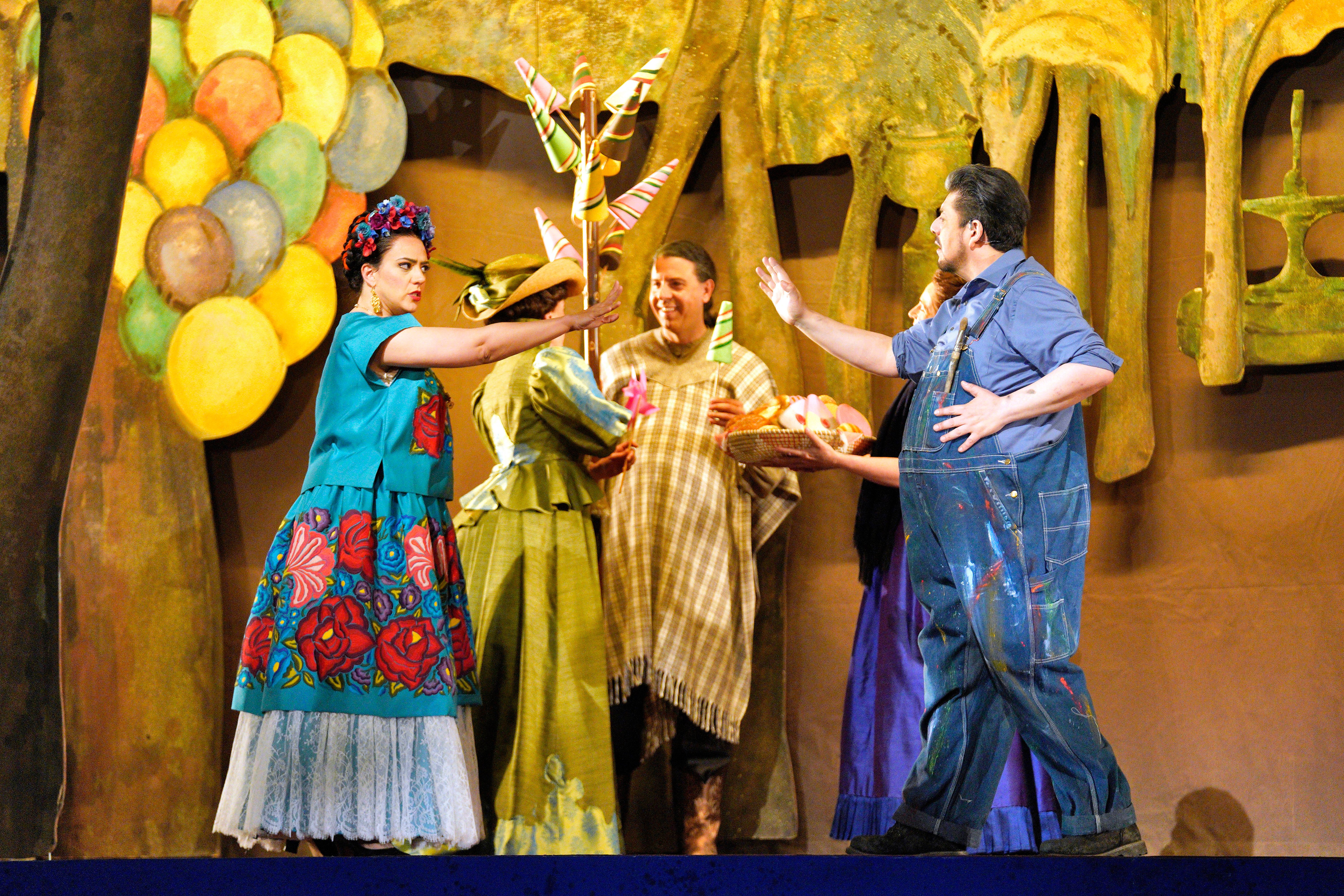 Scene from Frida of man in overalls reaching out to a woman in a colorful dress reaching out to him