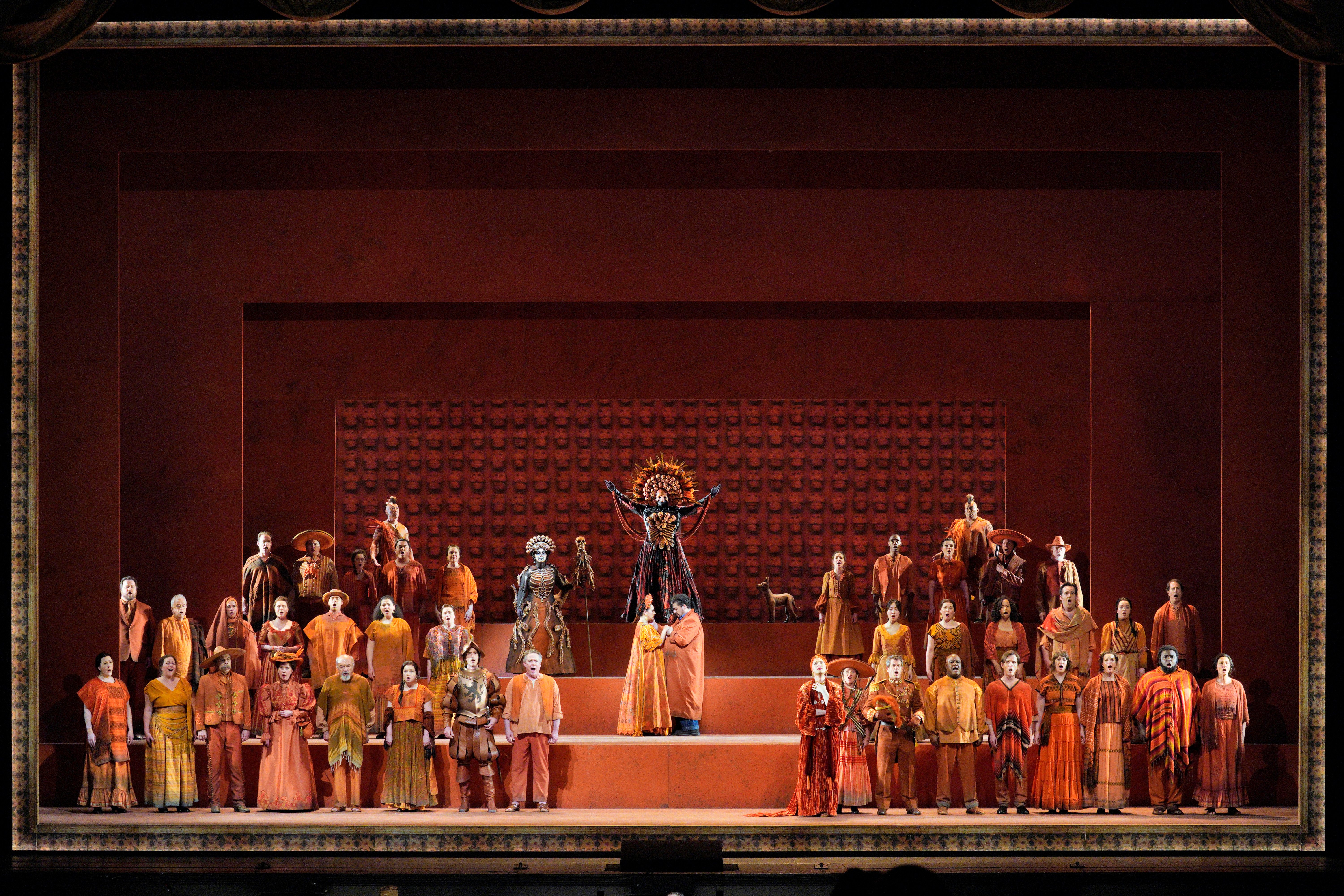 Scene from Frida of a group of people surrounding a man and woman holding hands facing each other while a person dressed in a ceremonial skeleton costume stands behind them with hands raised.